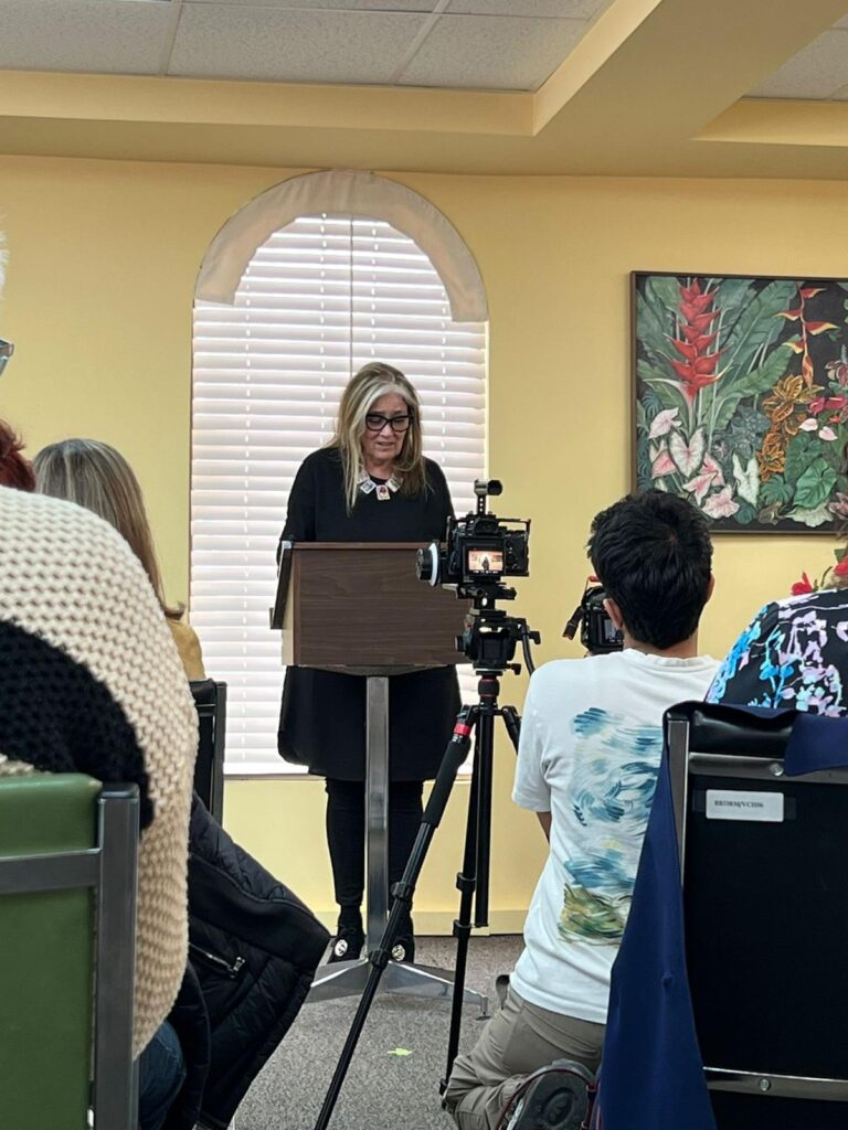 achel Manley, Governor General’s Award–winning author, stands at a podium inside the Jamaican Consulate General in Toronto, reading an excerpt from her book “George The Last” during its 2025 launch event.
